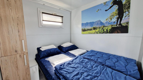 Slaapkamer op een woonboot met een dubbel bed, blauw beddengoed, houten kast en raam.