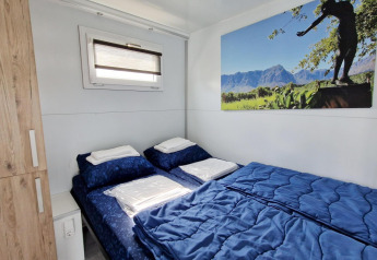 Houseboat bedroom with a double bed, blue bedding, wooden closet, small window, and wall art.