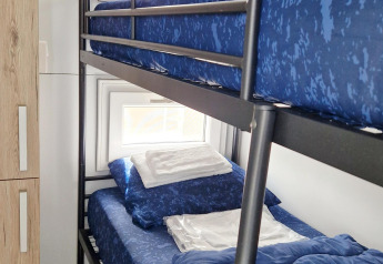 Stapelbed met blauw beddengoed op een woonboot, raam op de achtergrond en houten kast links ervan.