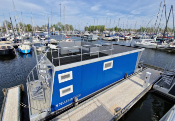 Husbåd Havenlodge N ved Marina Parcs Naarden, Holland, omgivet af lystbåde og fortøjningsbroer.