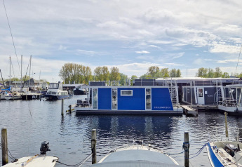 View of the Havenlodge N houseboat at Marina Parcs Naarden in the Netherlands on a bright day.