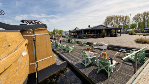 Menschen entspannen sich an einem Wassersteg mit Liegestühlen bei einer Glamping-Unterkunft und Restaurant.