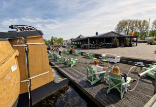 Menschen entspannen sich an einem Wassersteg mit Liegestühlen bei einer Glamping-Unterkunft und Restaurant.