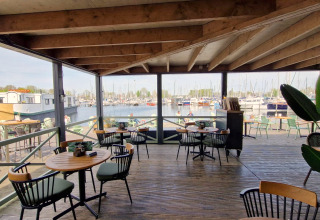 Blick von einer überdachten Terrasse mit Bistro-Tischen auf einen Yachthafen bei einer Glamping-Unterkunft.