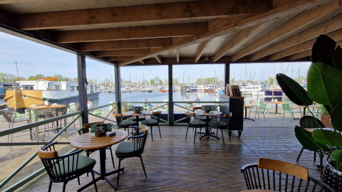 Vista desde una terraza cubierta con mesas de café hacia un puerto deportivo lleno de barcos en un glamping.