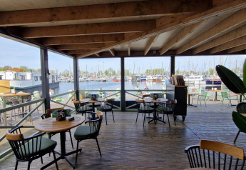 View from a covered terrace with café tables overlooking a marina full of boats at a glamping site.