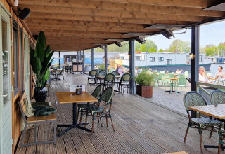 Overdekt terras op een woonboot met tafels en stoelen, met uitzicht op het water en boten.