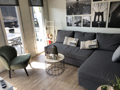 Acogedora sala de estar en una casa flotante en Marina Parcs Naarden con sofá gris, silla verde y arte mural.