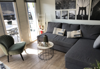 Acogedora sala de estar en una casa flotante en Marina Parcs Naarden con sofá gris, silla verde y arte mural.