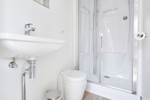 Moderne badkamer op een woonboot met witte wastafel, toilet en inloopdouche, licht en eigentijds.