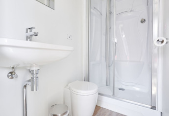 Moderne husbådsbadeværelse med hvid vask, toilet og brusekabine, minimalistisk og lyst design.