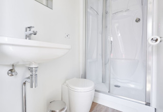 Moderne badkamer op een woonboot met witte wastafel, toilet en inloopdouche, licht en eigentijds.