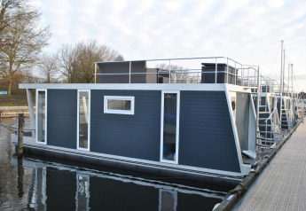 Modern houseboat named Havenlodge at Marina Parcs Naarden in the Netherlands, docked on calm water.