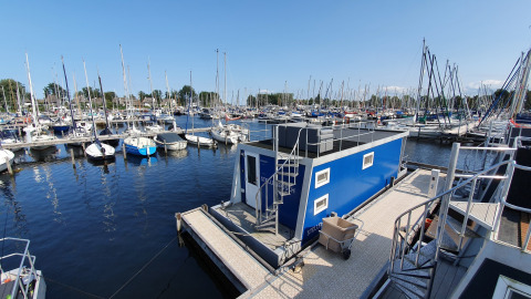 Casa flotante en Marina Parcs Naarden, Países Bajos, rodeada de muchos veleros y un cielo despejado.