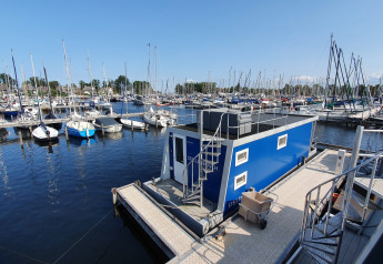 Husbåd ved Marina Parcs Naarden i Holland, omgivet af mange sejlbåde og blå himmel.