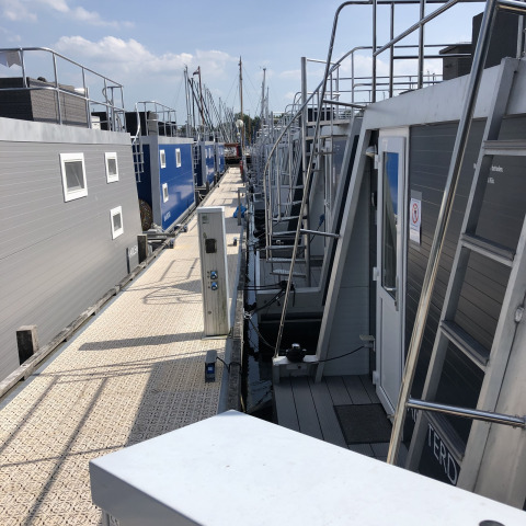 Houseboats docked along a floating pier at Marina Parcs Naarden in the Netherlands on a sunny day.