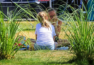 Twee mensen genieten van een picknick in het gras bij Sunlodge op vakantiepark 't Rheezerwold, Nederland.