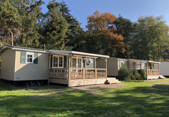 Family chalets with porches at Kampeerdorp de Zandstuve in the Netherlands, surrounded by trees and sun.