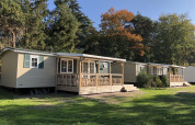 Family chalets with porches at Kampeerdorp de Zandstuve in the Netherlands, surrounded by trees and sun.