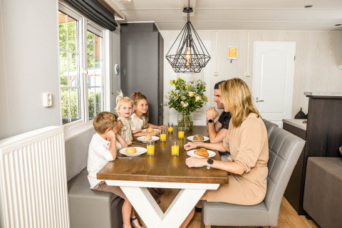 Una famiglia fa colazione insieme al tavolo in uno chalet luminoso a Kampeerdorp de Zandstuve, Paesi Bassi.