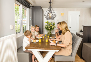 Una famiglia fa colazione insieme al tavolo in uno chalet luminoso a Kampeerdorp de Zandstuve, Paesi Bassi.