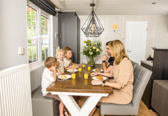 Una famiglia fa colazione insieme al tavolo in uno chalet luminoso a Kampeerdorp de Zandstuve, Paesi Bassi.