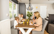Eine Familie frühstückt gemeinsam an einem Tisch in einem hellen Chalet im Kampeerdorp de Zandstuve, Niederlande.