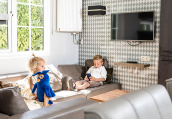 Two children relaxing in a cozy family chalet lodge at Kampeerdorp de Zandstuve, Netherlands, with toys.