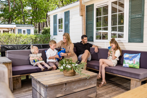 Familia relajándose en el porche de un chalet en Kampeerdorp de Zandstuve, Países Bajos, disfrutando al aire libre.