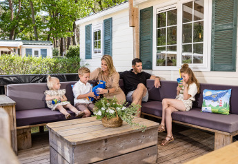 Familia relajándose en el porche de un chalet en Kampeerdorp de Zandstuve, Países Bajos, disfrutando al aire libre.