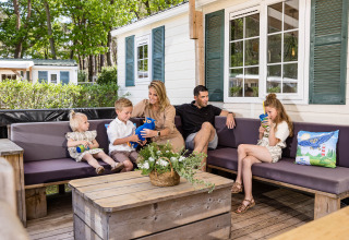 Familie sitzt auf der Terrasse einer Hütte im Kampeerdorp de Zandstuve, Niederlande, und genießt das Beisammensein.