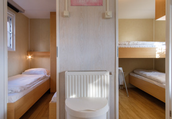 Vue intérieure d'une chambre familiale en chalet à Kampeerdorp de Zandstuve aux Pays-Bas avec trois lits simples.