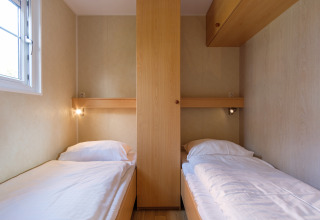 Two single beds with white bedding in a compact wooden room at Family chalet in Kampeerdorp de Zandstuve.