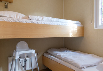 Moderne familieværelse på Kampeerdorp de Zandstuve med køjesenge og høj stol ved vindue.