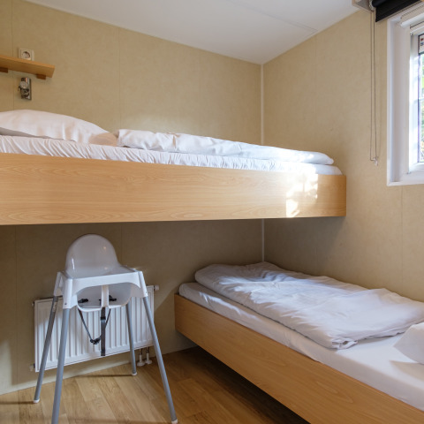 Moderne familieværelse på Kampeerdorp de Zandstuve med køjesenge og høj stol ved vindue.