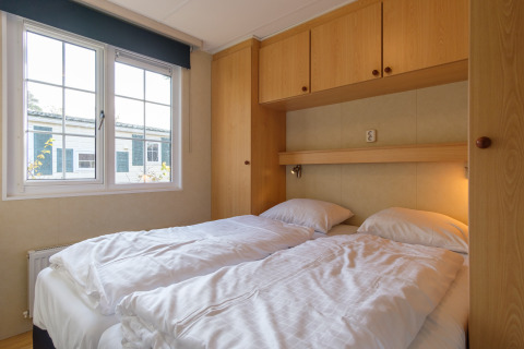Dormitorio con dos camas individuales y armarios de madera en Family chalet, Kampeerdorp de Zandstuve, Países Bajos.