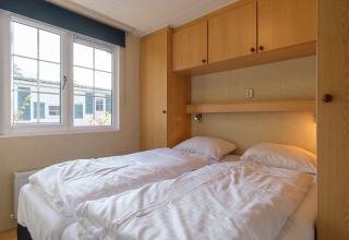 Dormitorio con dos camas individuales y armarios de madera en Family chalet, Kampeerdorp de Zandstuve, Países Bajos.