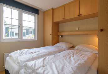 Bedroom with two single beds and wood cabinets at the Family chalet, Kampeerdorp de Zandstuve, Netherlands.