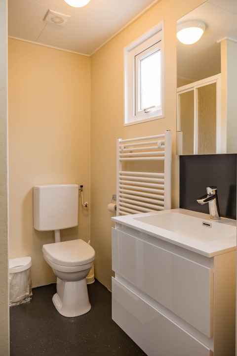 Bagno moderno al Family Chalet con wc, lavabo bianco, specchio, scaldasalviette e una piccola finestra.