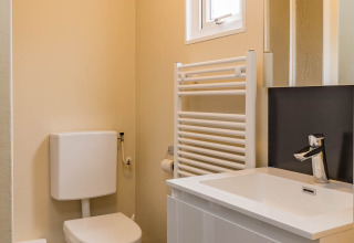 Baño moderno en Family Chalet con inodoro, lavabo blanco, espejo, radiador toallero y ventana pequeña.