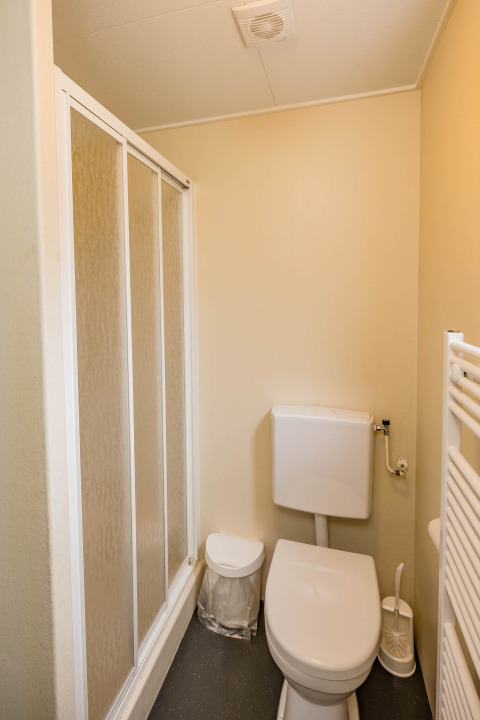 Petite salle de bains avec douche, toilettes, poubelle et brosse dans une cabane familiale à Zandstuve.