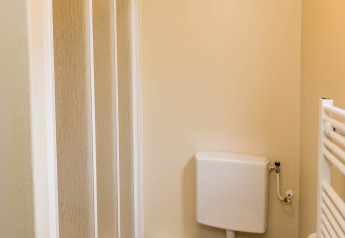 Small bathroom with shower, toilet, waste bin and toilet brush in a family chalet at Zandstuve lodge.