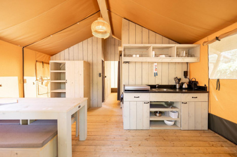 Binnenzicht van de Villatent Nomad safaritent met houten meubels, keuken en warme, natuurlijke verlichting.