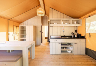 Binnenzicht van de Villatent Nomad safaritent met houten meubels, keuken en warme, natuurlijke verlichting.