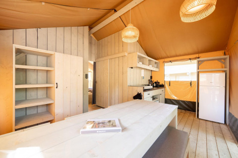 Binnenkant van een safari tent Villatent Nomad met houten meubels, keuken en koelkast in warme sfeer.