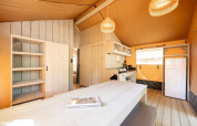 Interior de una tienda safari Villatent Nomad con muebles de madera, cocina y frigorífico bajo luz cálida.