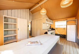 Interno della tenda safari Villatent Nomad con arredi in legno, cucina attrezzata e frigorifero.