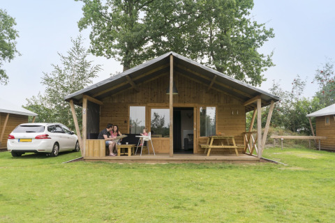 Family relaxing on the porch of a Rheezerlodge safari tent at Kampeerdorp de Zandstuve in the Netherlands.