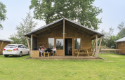 Familie ontspant op het terras van een Rheezerlodge safaritent in Kampeerdorp de Zandstuve, Nederland.