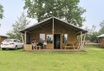 Familie nyder udendørs på verandaen af Rheezerlodge safaritelten ved Kampeerdorp de Zandstuve, Holland.